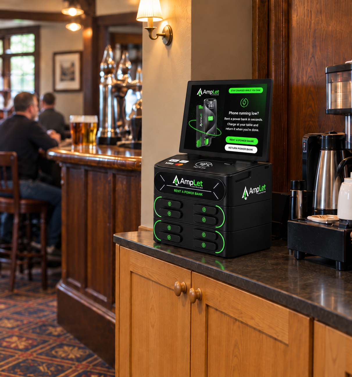 An AmpLet charging station on a wooden service cabinet beside a pub coffee machine, facing into the aisle.